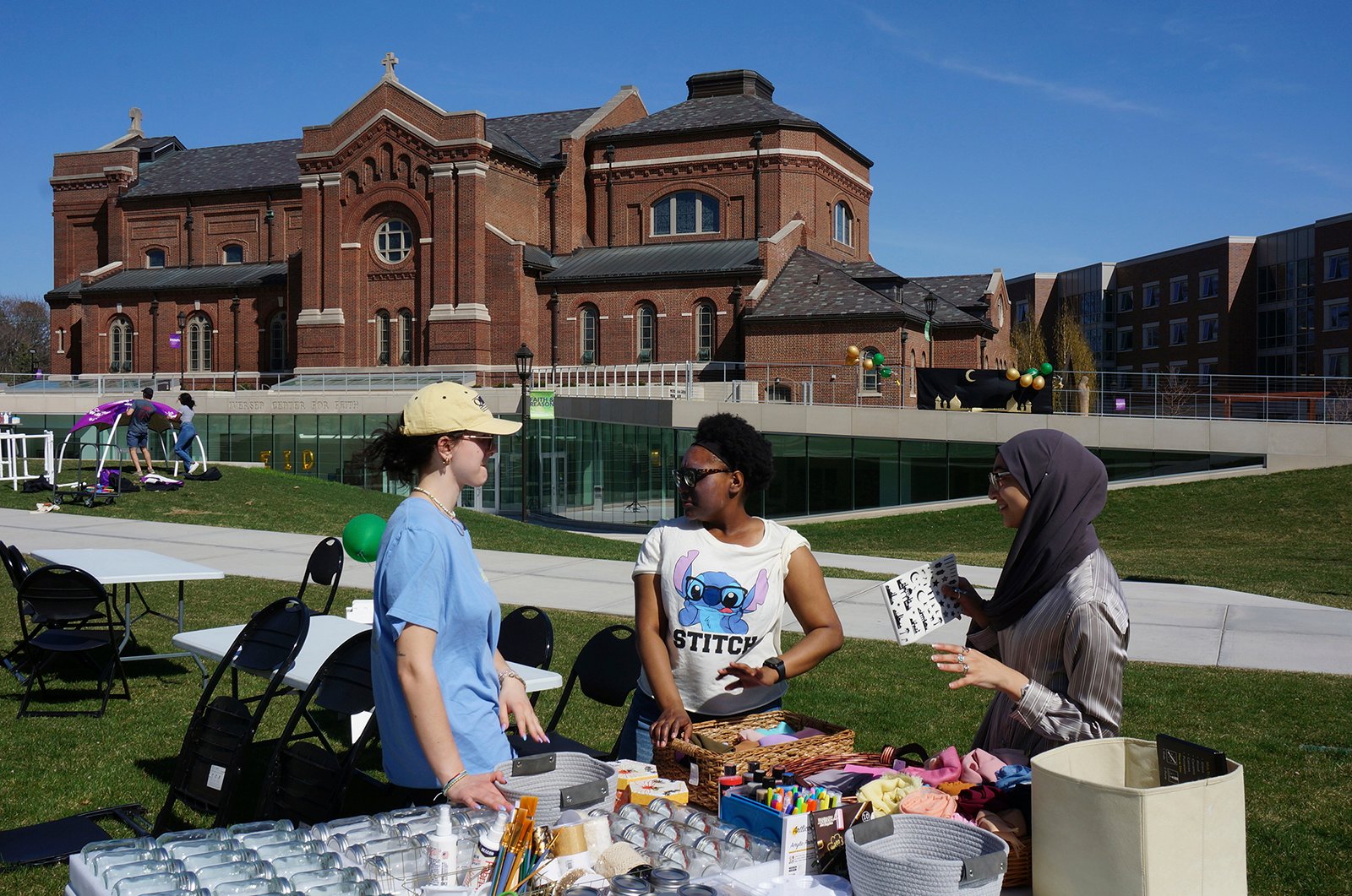 From left, University of St. Thomas students Helen Knudson, Arianna Norals, and Salma Nadir set up a table for decorating mason jars and headscarves at the school's celebration for the end of the Muslim holy month of Ramadan on the lawn in front of the Catholic chapel in St. Paul, Minn., on Saturday, May 7, 2022. Campus ministry helped organize the event, which included similar stress-reducing activities, as many faith leaders across US campuses seek ways to help students manage stress and anxiety. (AP Photo/Giovanna Dell'Orto)
