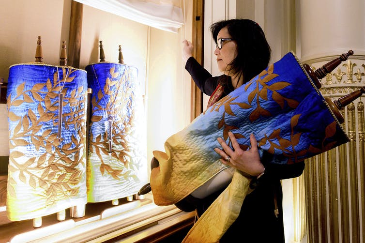 A woman removes a Torah scroll from the ark, a cabinet that houses scrolls of the Hebrew Bible.